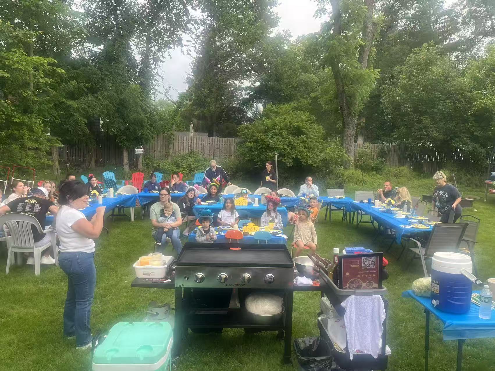 Large backyard family party with blue tablecloths and Blackstone grill in the foreground